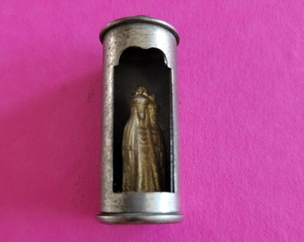 以下が含まれることがあります： 銀色の金属製の容器の中に、小さな金色の女性の像が入っています。像は容器の透明な窓から見ることができます。