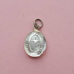 May include: Silver oval charm with a cross and the text "LA VIE CROIX" and "GRACE EUCHARISTIE" around the cross. The charm has the number "3204" on the bottom.