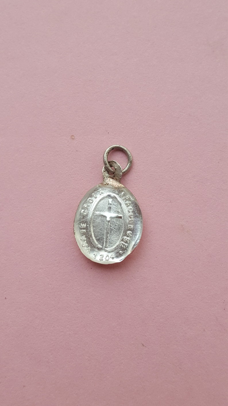 May include: Silver oval charm with a cross and the text "LA VIE CROIX" and "GRACE EUCHARISTIE" around the cross. The charm has the number "3204" on the bottom.