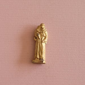 Könnte beinhalten: Eine kleine goldfarbene Figur eines Heiligen, der ein Kind hält. Die Figur ist etwa 5 cm hoch und hat ein detailliertes Design. Der Sockel der Figur ist mit dem Wort "ZANCHINI" beschriftet.