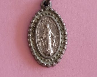 Puede incluir: Pendiente ovalado de plata con una representación de la Virgen María y el texto "CONCEIVED WITHOUT SIN PRAY FOR US" alrededor de la imagen.
