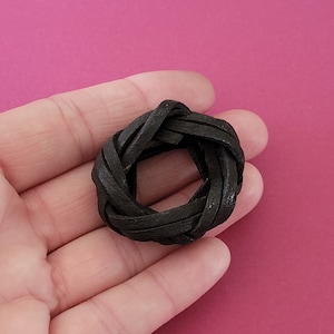 May include: A black leather ring, braided into a circular shape, is held in a hand.