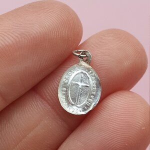 May include: A silver oval-shaped pendant with a cross and the inscription "Ave Gratia Plena" around the edge.