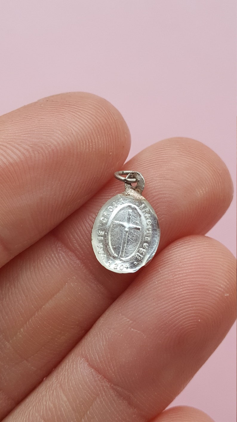 May include: A silver oval-shaped pendant with a cross and the inscription "Ave Gratia Plena" around the edge.