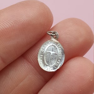 May include: Silver oval charm with a cross and the inscription "Ave Maria Gratia Plena" around the edge.
