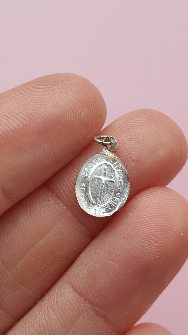 May include: Silver oval charm with a cross and the inscription "Ave Maria Gratia Plena" around the edge.