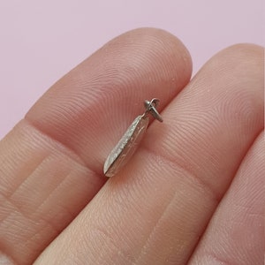 May include: A silver pendant shaped like a teardrop with a textured surface.