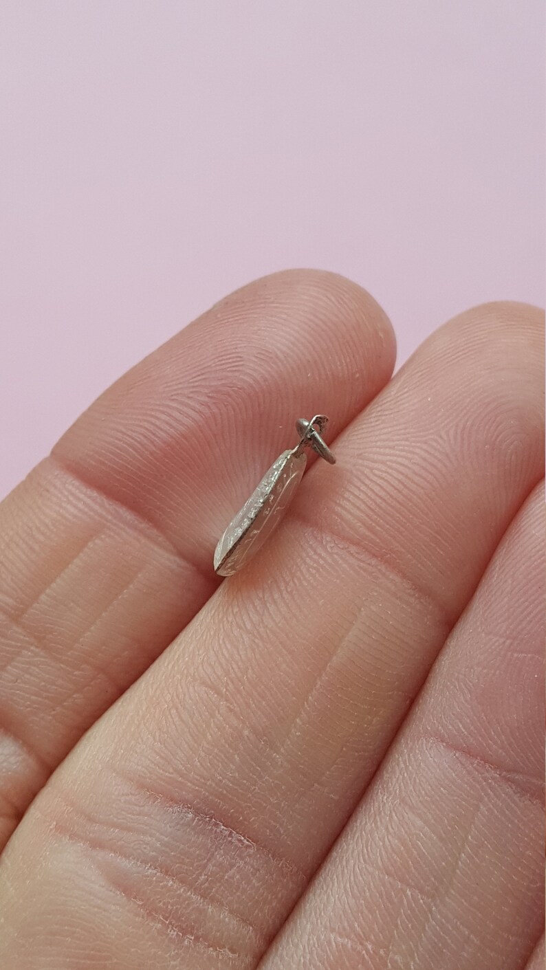 May include: A silver pendant shaped like a teardrop with a textured surface.