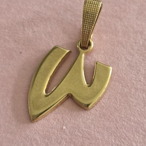 May include: A gold-toned metal pendant shaped like the lowercase letter w. The pendant features a smooth, polished surface and includes a textured, rectangular bail at the top for attaching to a chain or necklace, presented in a simple design.