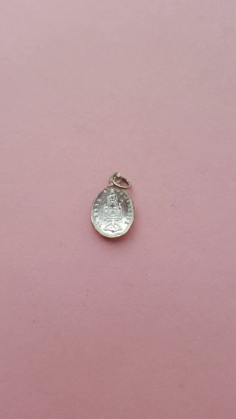 May include: Silver charm with a detailed design of a building with a dome and a cross on top. The charm is oval shaped and has a loop at the top for attaching to a chain or bracelet.