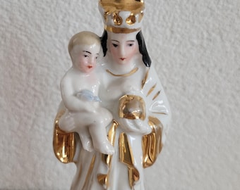 May include: A white porcelain figurine of the Virgin Mary holding a baby Jesus. The figurine is decorated with gold paint and has a crown on Mary's head.