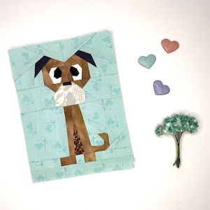 May include: A paper pieced quilt block featuring a brown and white dog with a light blue background. The dog is standing on its hind legs with its front paws raised. The background is a light blue fabric with a white pattern.