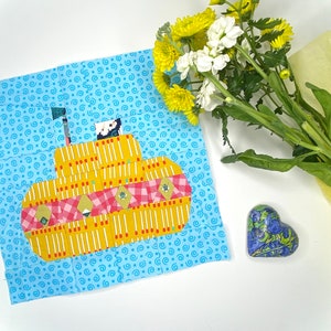 May include: A yellow submarine applique with red and white checkered details on a blue background with a white swirl pattern.