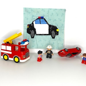 May include: A red fire truck with a yellow ladder, a black and white police car, a red sports car, and two toy people. The police car is on a blue and white fabric background.