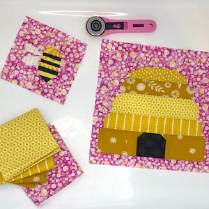 Puede incluir: Un conjunto de cuadrados de tela con un diseño de abeja y panal. Los cuadrados son de color rosa con lunares blancos y patrones amarillos y blancos. La abeja es negra y amarilla.
