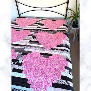 May include: A pink and black patchwork quilt with a geometric design. The quilt is made from various fabrics, including a pink fabric with white polka dots, a black and white geometric fabric, and a black and white floral fabric.