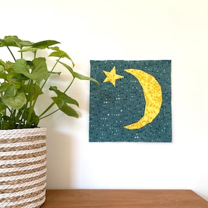 May include: A yellow crescent moon and a five-pointed star on a blue background with white polka dots. The moon and star are made of fabric and are sewn onto the blue fabric.