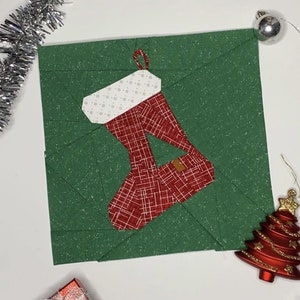 Peut inclure: Une chaussette de Noël rouge et blanche sur un fond vert. La chaussette est en tissu et a un motif à carreaux. Le fond est un tissu vert avec une texture scintillante.