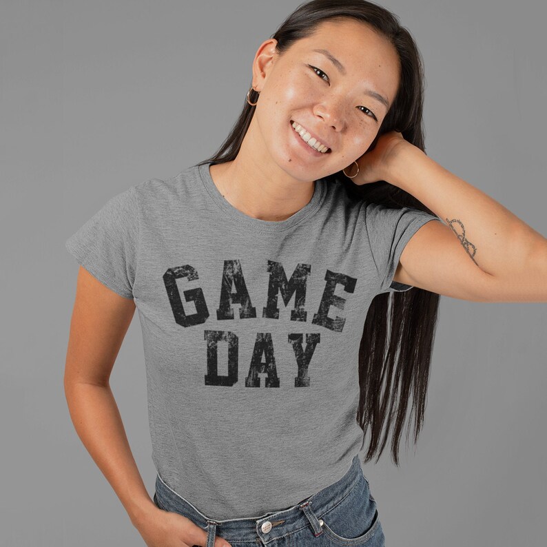 May include: A heather grey t-shirt with the text "GAME DAY" printed in black distressed lettering.