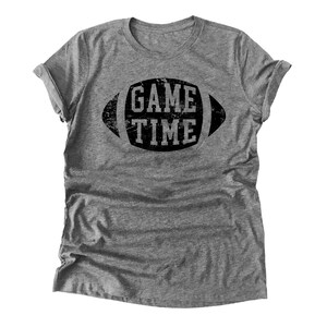Puede incluir: Una camiseta gris jaspeada con un gr&aacute;fico negro desgastado de un bal&oacute;n de f&uacute;tbol con el texto "GAME TIME" en su interior.