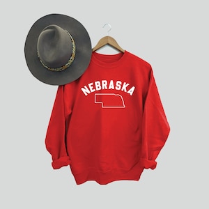 May include: Red sweatshirt with white text that says "NEBRASKA" and an outline of the state of Nebraska.