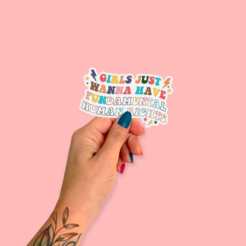 K&ouml;nnte beinhalten: Ein Aufkleber mit dem Text "Girls Just Wanna Have Fundamental Human Rights" in einem Regenbogen aus Farben mit Blitzen und Sternen.