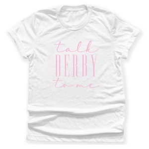 Puede incluir: Camiseta blanca con la frase "talk DERBY to me" en rosa. El texto est&aacute; escrito en cursiva. La camiseta tiene cuello redondo y mangas cortas. El texto est&aacute; centrado.