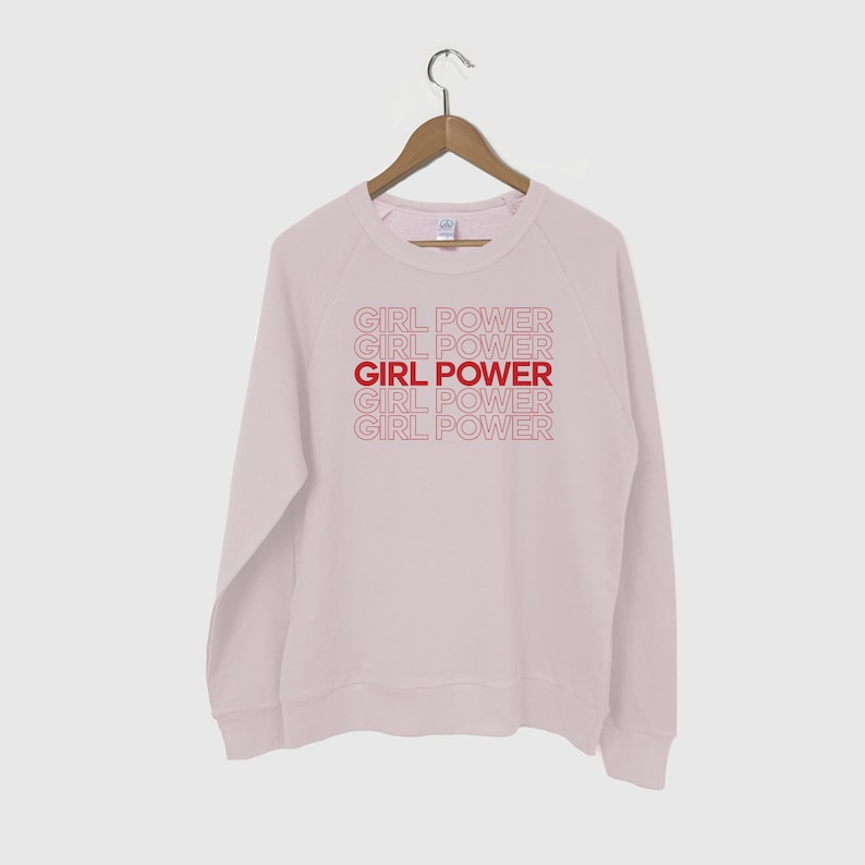 May include: A light pink sweatshirt with the phrase "GIRL POWER" repeated five times in red outlined text.