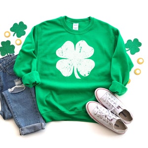May include: Green sweatshirt with a white distressed four-leaf clover graphic.