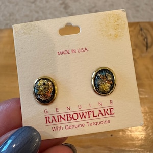 May include: A pair of oval stud earrings with gold-toned rims, featuring dark centers embedded with metallic gold and copper flakes. The earrings are attached to a cream-colored display card printed with the text MADE IN U.S.A. and RAINBOWFLAKE.