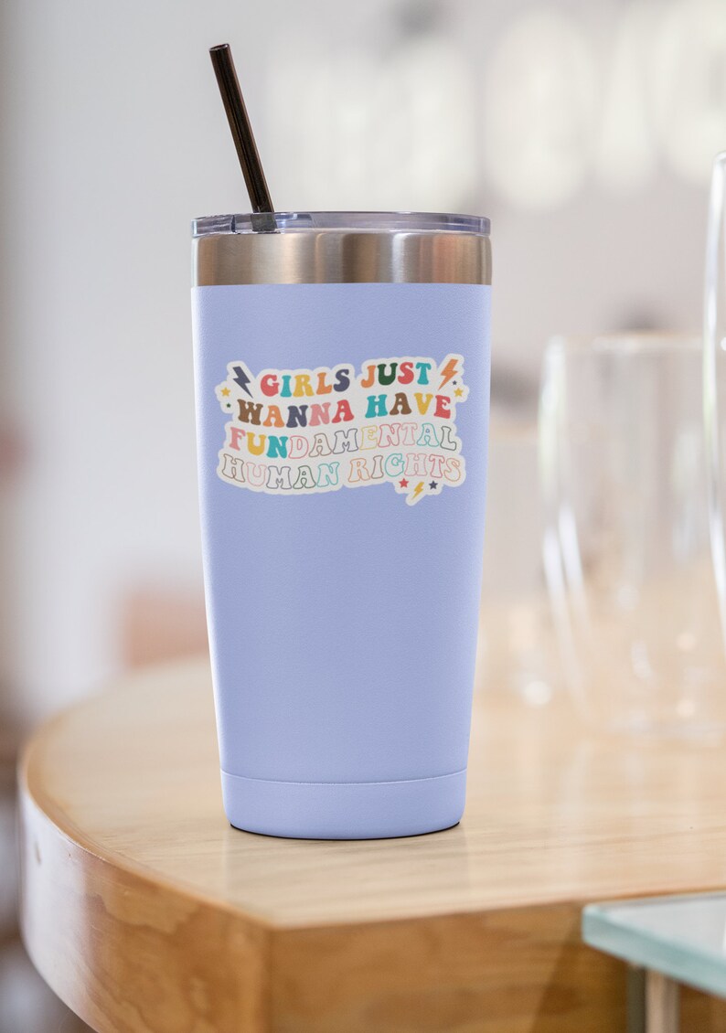 K&ouml;nnte beinhalten: Ein hellblauer Edelstahlbecher mit einem Aufkleber, auf dem "Girls Just Wanna Have Fundamental Human Rights" in bunten Buchstaben mit Sternen und Blitzen steht.