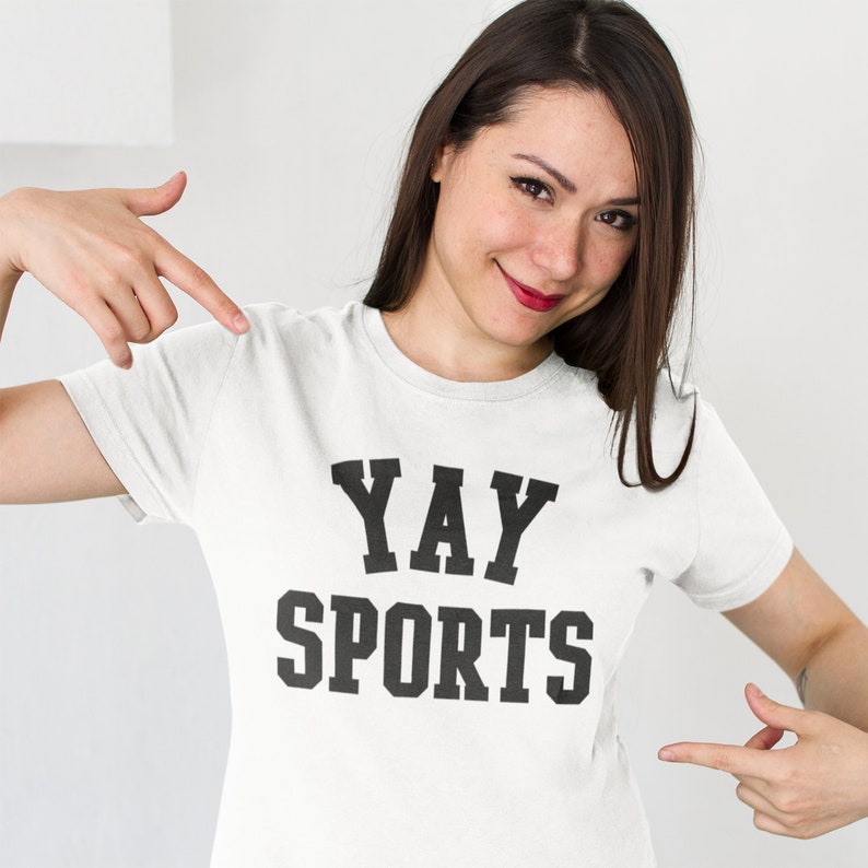 May include: White t-shirt with black text that reads "YAY SPORTS" in a collegiate font.