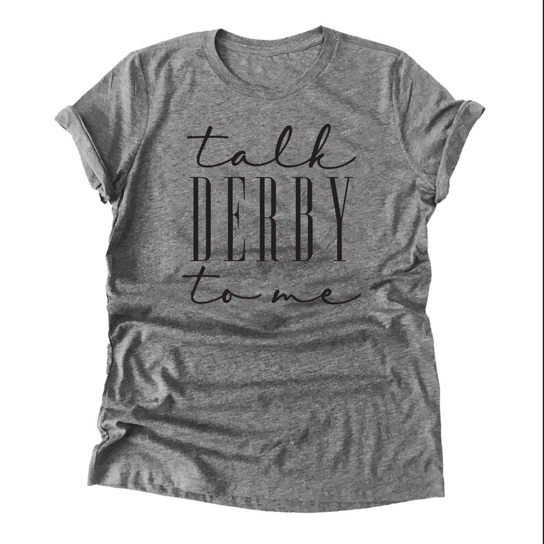 Puede incluir: Una camiseta gris jaspeada con mangas enrolladas. La frase "talk DERBY to me" est&aacute; impresa en negro con letras cursivas y en bloque. La camiseta informal probablemente est&aacute; hecha de un material suave y c&oacute;modo.