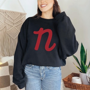 May include: A black sweatshirt with a red cursive letter "n" on the front.
