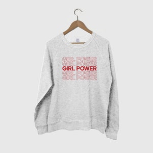 May include: A gray sweatshirt with the phrase "GIRL POWER" repeated five times in red lettering. The text is stacked vertically in a retro style.