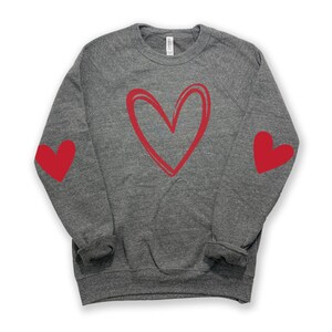 May include: A gray sweatshirt with a red heart design on the front and red hearts on the elbows.