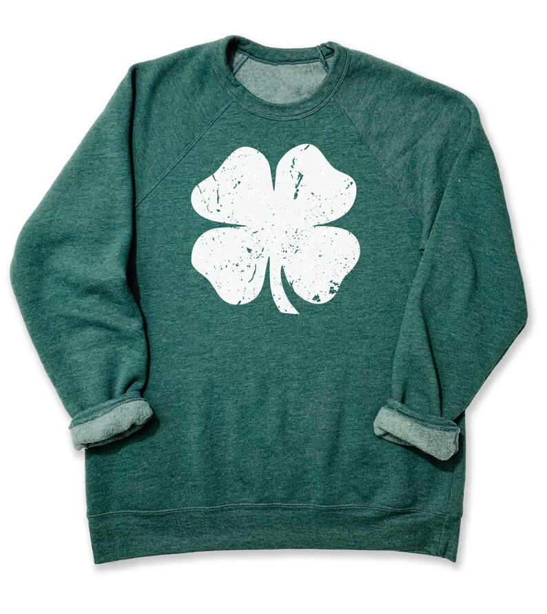 May include: A green sweatshirt with a white distressed four-leaf clover graphic.