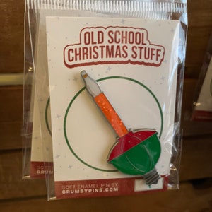 Puede incluir: Un pin de esmalte verde, rojo y blanco con forma de bombilla de Navidad antigua. El pin dice "Old School Christmas Stuff" y "Soft Enamel Pin by Crumbypins.com".
