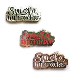 May include: Three gold-colored pins with the text "Son of a Nutcracker" in black, red, and white lettering.