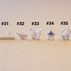 May include: A set of 7 silver earrings with different designs, including a sun, a bar, a bird, a butterfly, a star, a flower, and a star. The earrings are numbered 30 through 36.