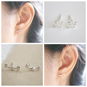 May include: Four different pairs of silver earrings. The first pair is a simple bar, the second pair is a small flower, the third pair is a row of three stars, and the fourth pair is a small branch.