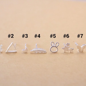 May include: Eight silver stud earrings with different designs, including a bow, triangle, heart, feather, bunny, stars, butterfly, and heart. The earrings are numbered 1 through 8.