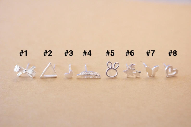 May include: Eight silver stud earrings with different designs, including a bow, triangle, heart, feather, bunny, stars, butterfly, and heart. The earrings are numbered 1 through 8.