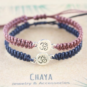 May include: Two friendship bracelets with brown and black cords, tied with a silver Om symbol charm.