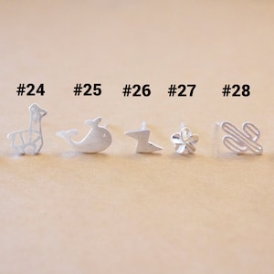 May include: Nine silver earrings with different designs, including an elephant, a giraffe, a whale, a lightning bolt, a flower, a cactus, and a daisy. The earrings are numbered 23 through 29.