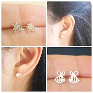 May include: Four pairs of silver stud earrings. The first pair features a cluster of five stars. The second pair features a butterfly. The third pair features a single flower. The fourth pair features two bees.