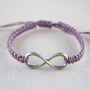 May include: A handmade macrame bracelet in a muted purple color, featuring a bronze-colored infinity symbol. The bracelet is adjustable with sliding knots, offering a comfortable fit. This accessory is perfect for everyday wear.