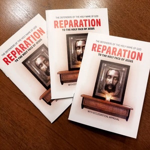 May include: Three white pamphlets with the title "Reparation to the Holy Face of Jesus" printed in red. The pamphlets feature an image of Jesus' face in a frame on a wooden stand. The text "With Ecclesiastical Approval" is printed at the bottom of the pamphlet.