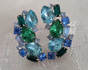 May include: A pair of clip-on earrings with a cluster of blue and green rhinestones. The earrings are made of metal and have a silver finish.