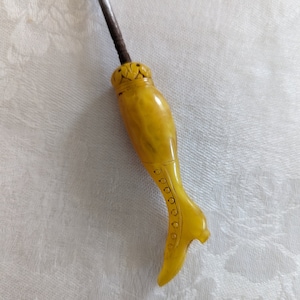 May include: A yellow, carved, boot-shaped,  decorative sewing thimble with a metal needle.